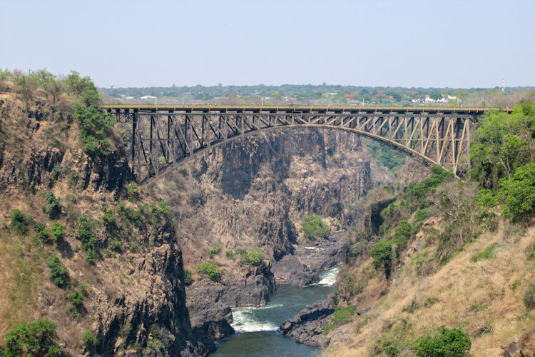 The image depicts a traditional Leya village featuring thatched roof huts, with community members dressed in vibrant attire performing a cultural dance. This lively scene reflects the rich culture of the Zambian people, making it a captivating tourist attraction in the Livingstone region, near the magnificent Victoria Falls.