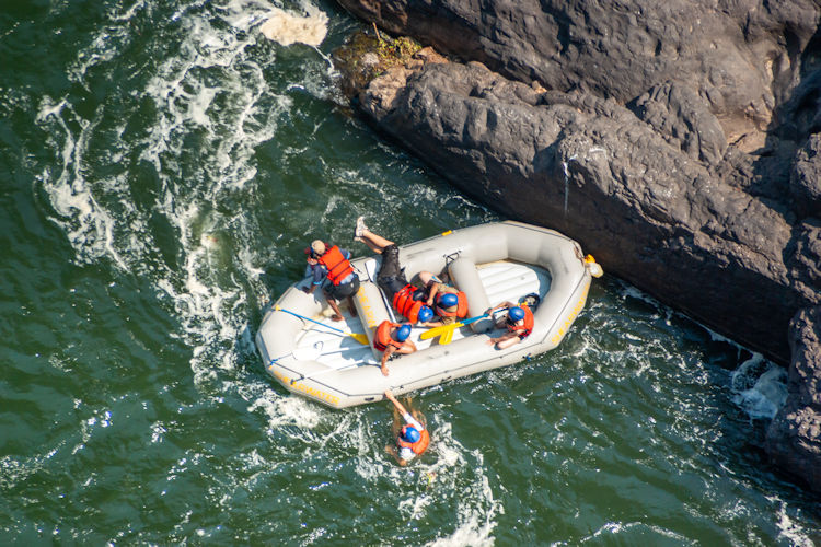 A team of adventurers is white water rafting through the thrilling rapids of the Batoka Gorge, surrounded by towering canyon walls on both sides. The scene captures the adrenaline rush of navigating the Zambezi River, a popular spot for tourists seeking adventure near Victoria Falls.