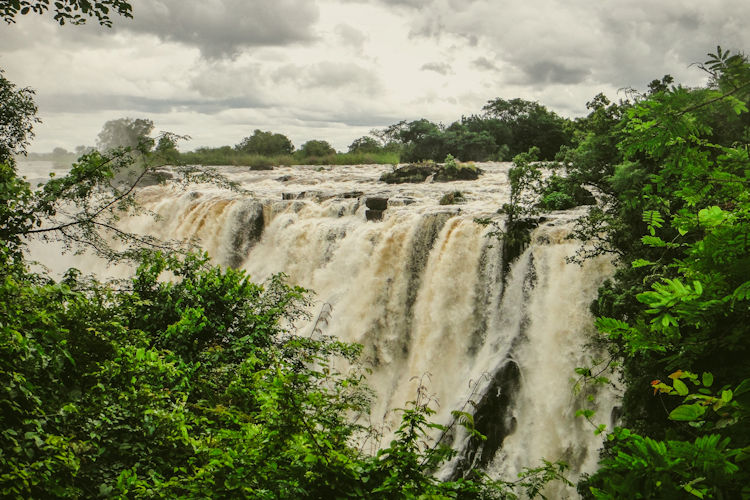 A group of adventurous swimmers is seen at the edge of Devil's Pool, peering over the breathtaking drop of Victoria Falls, with the mighty Zambezi River cascading below. This thrilling experience is part of the iconic attractions in Victoria Falls, located in Zimbabwe.