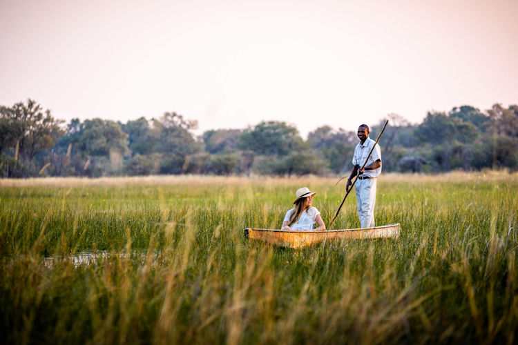 A traditional mokoro, or dugout canoe, glides smoothly through the serene waters of Botswana's Okavango Delta, flanked by lush papyrus reeds on either side, creating a tranquil atmosphere perfect for wildlife viewing. This peaceful scene captures the essence of safari experiences in one of the world's UNESCO World Heritage Sites, where visitors can enjoy the beauty of nature and abundant bird life.