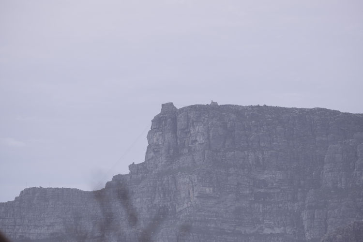 An aerial view showcases Table Mountain, a prominent landmark in Cape Town, with a rotating cable car ascending against a clear blue sky. This stunning scene highlights the beauty of the Mother City, surrounded by the Atlantic Ocean and offering breathtaking views of the surrounding coastal towns and iconic landscapes.