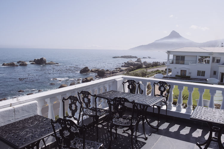A picturesque scene of a white sand beach lined with palm trees, with the dramatic mountain buttresses of Table Mountain rising majestically in the background, embodying the stunning views that Cape Town, the Mother City of South Africa, is famous for. This idyllic coastal landscape invites visitors to explore the nearby attractions, including the iconic beaches and hiking trails of the Cape Peninsula.