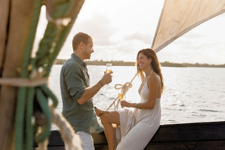 A romantic candlelit dinner table is elegantly set on a pristine white sand beach, with the Indian Ocean gently lapping at the shore and a stunning sunset painting the sky in vibrant hues. This intimate scene captures the essence of a dream honeymoon safari, perfect for couples looking to create unforgettable memories in one of the most romantic destinations in East Africa.