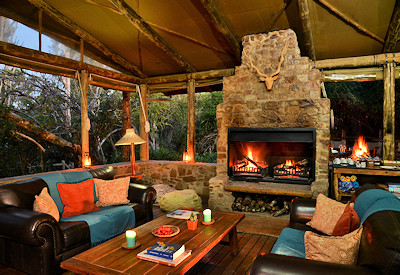 Open-air thatched lounge with grand fireplace at Sibuya River Camp Sibuya Game Reserve