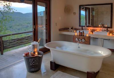 Large en-suite bathroom with bathtub and outdoor shower at AndBeyond Phinda Mountain Lodge Zululand